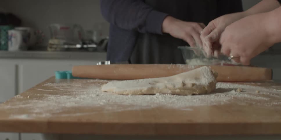 Two people are rolling out dough to make cookies