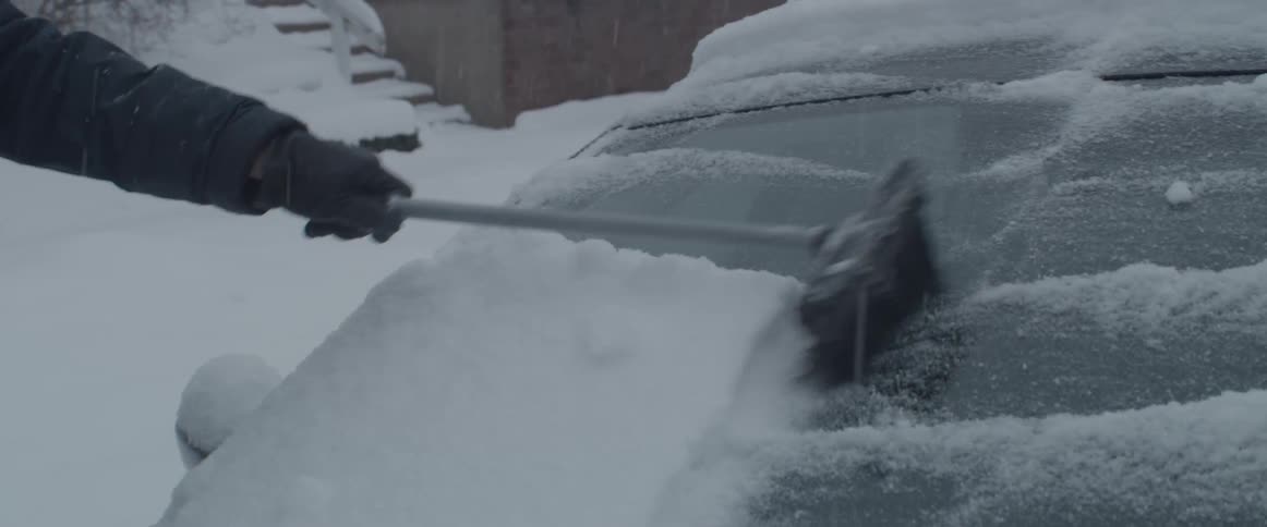 A man cleaning snow off of his car windshield