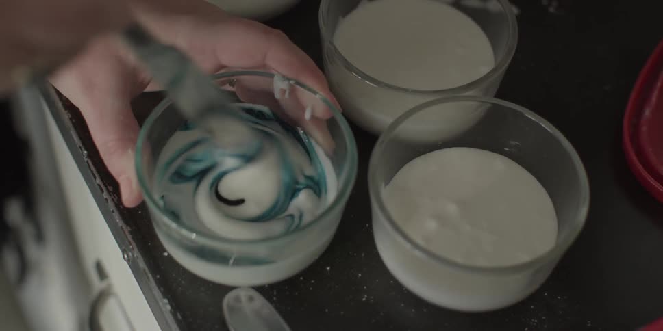 A person squeezed food coloring into a glass then mixes it