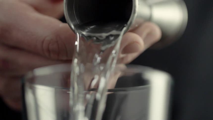 A bartender pours from a shot glass into a tumbler