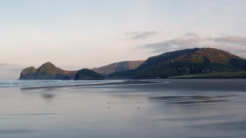 Mountains sit near the water as waves roll in