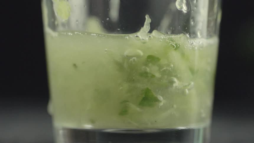 Liquid is being poured into a glass containing small chopped green pieces