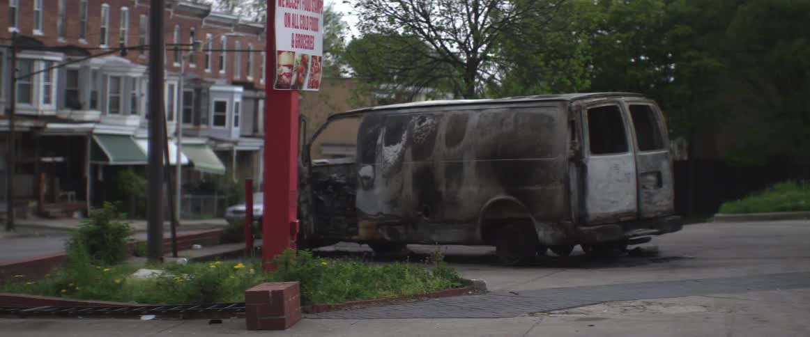 A burned out van sits in a lot on an urban street