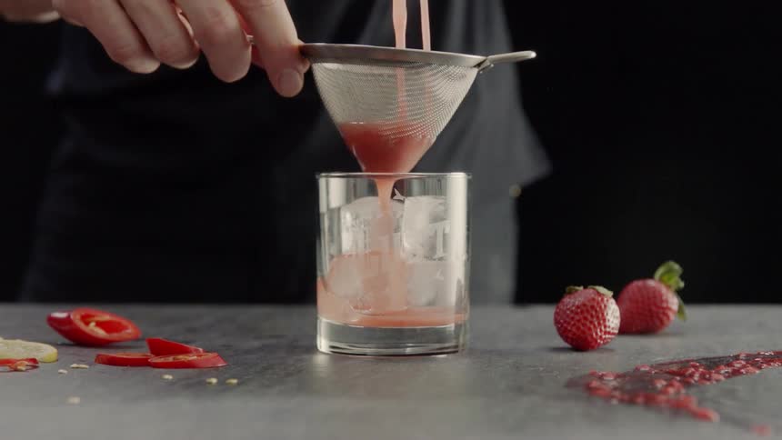 A person pours juice into a strainer into a glass