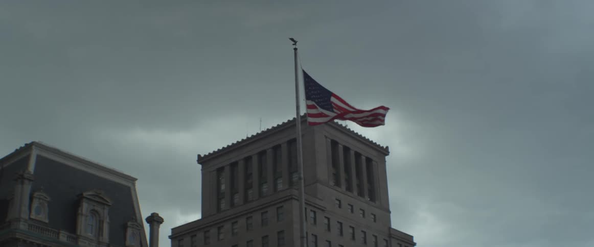 An american flag waves in the wind in front of some buildings on an overcast day