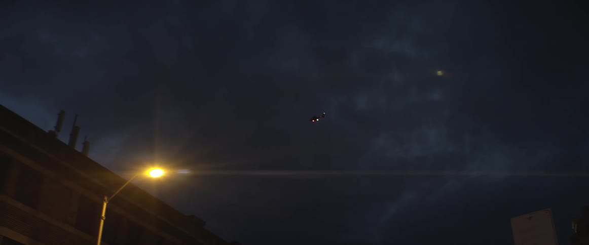 A helicopter flies over a building in the cloudy sky