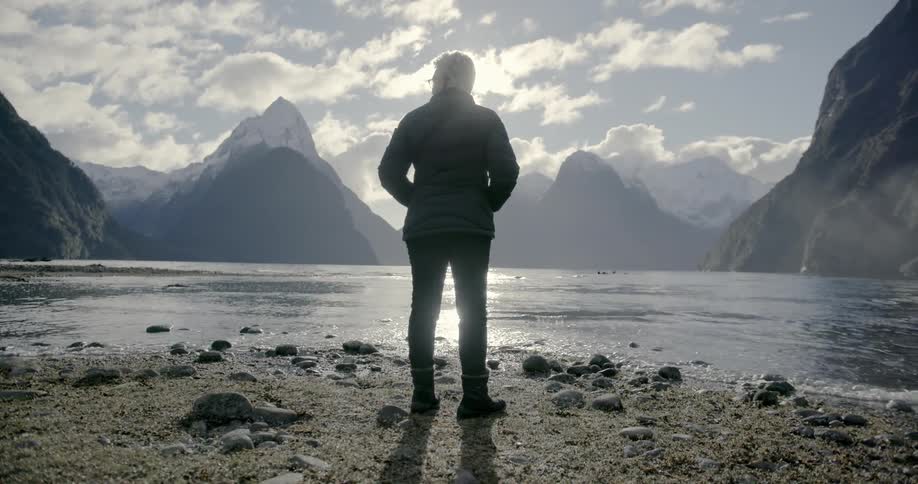 A woman stands on a rocky beach