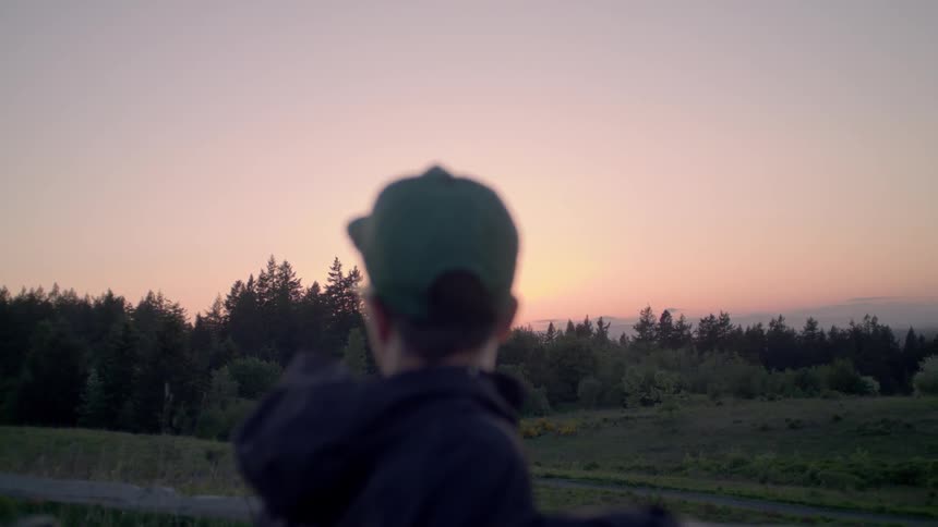 A man in a ball cap looks around a field at sunset