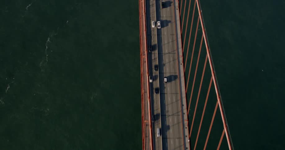 Cars driving over Golden Gate, with ships passing under