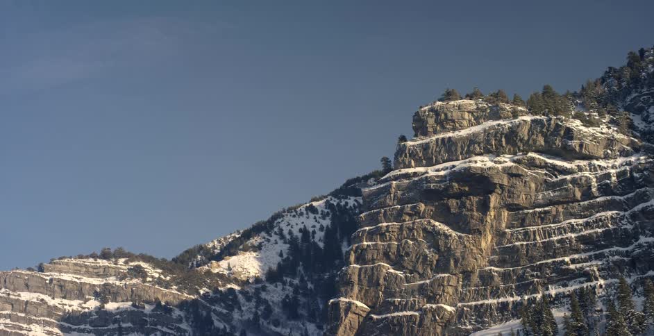 The mountain has some trees and is covered with snow