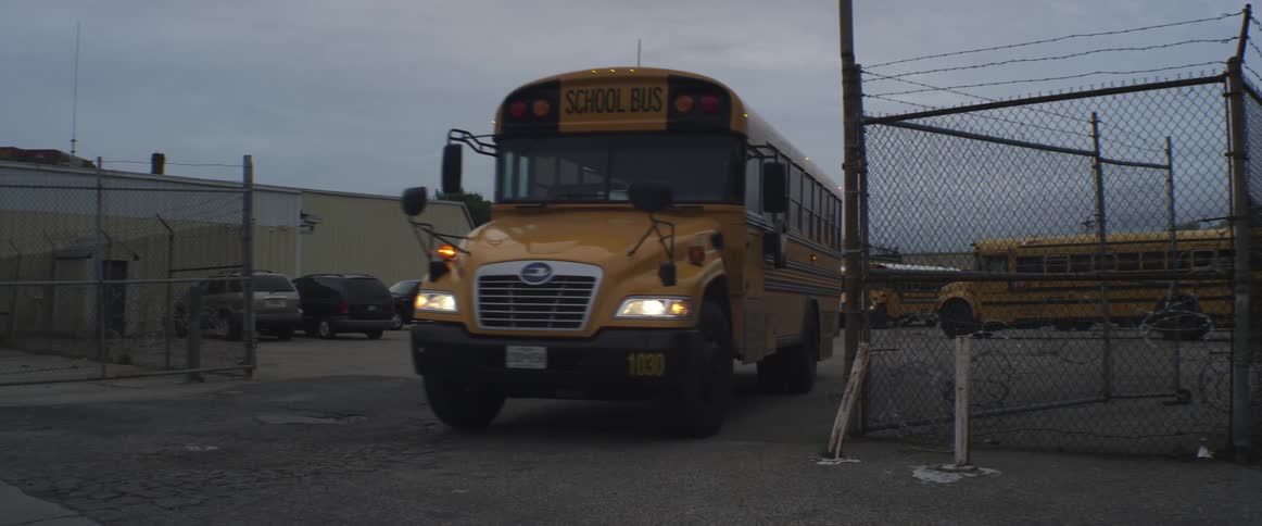 School bus leaving lot area through opened fence