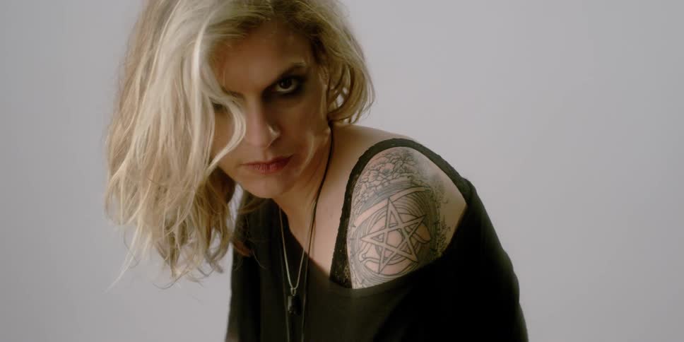 A woman with tattoos is playing with her hair and looking at the camera