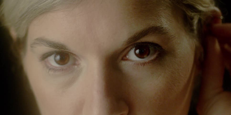 A woman blinks and fusses with her hair as she looks straight ahead