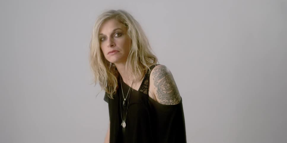 A woman pulls her shirt off her shoulder to reveal her tattoo