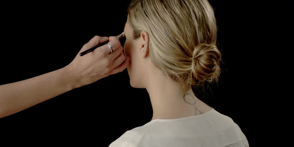 A woman is having makeup put on with a black background behind her