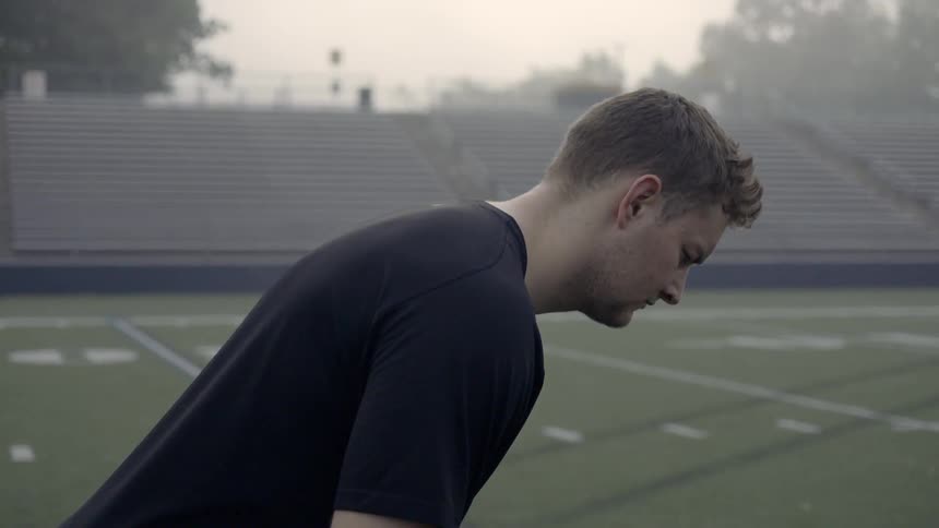 A man stands bent forward on a football field