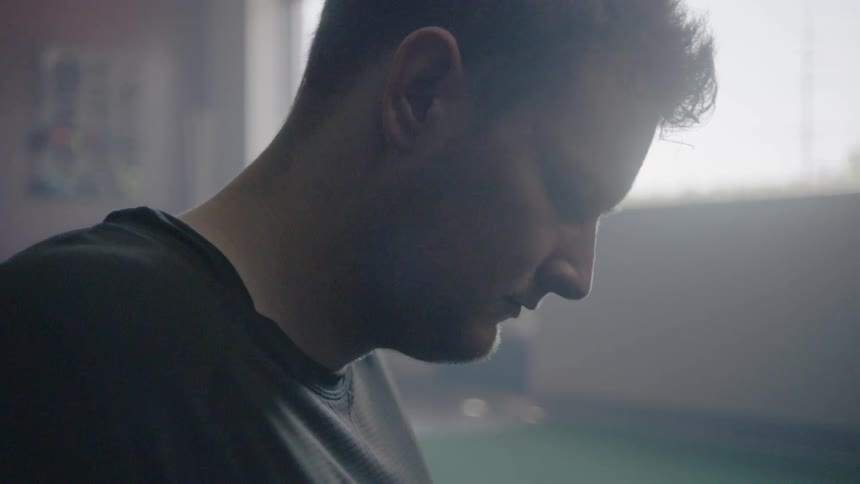 A man is breathing heavy and looking downwards while inside during the day