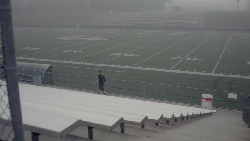 A man is walking past a set of bleachers in a football stadium