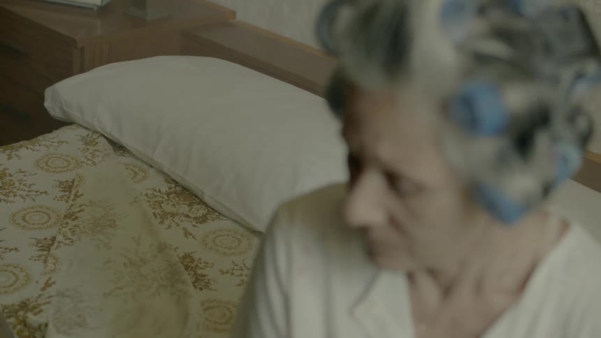 A woman wearing hair curlers turns in bed