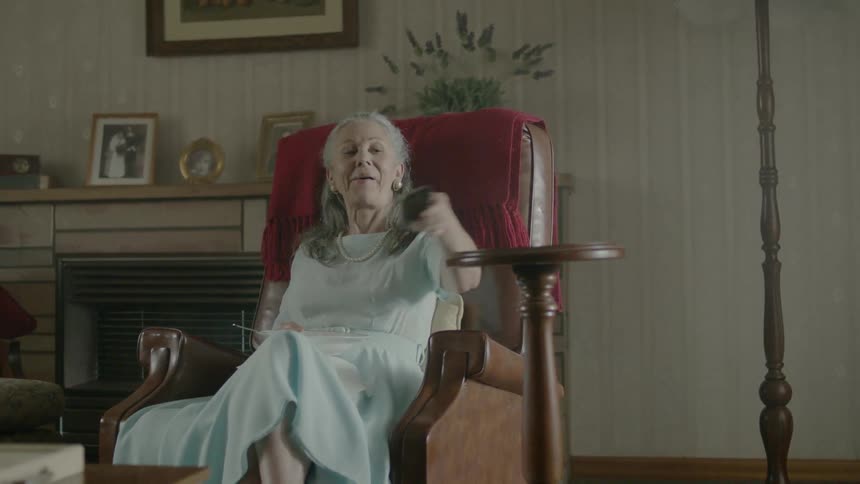 A woman is sitting in a chair, turning on the tv and eating