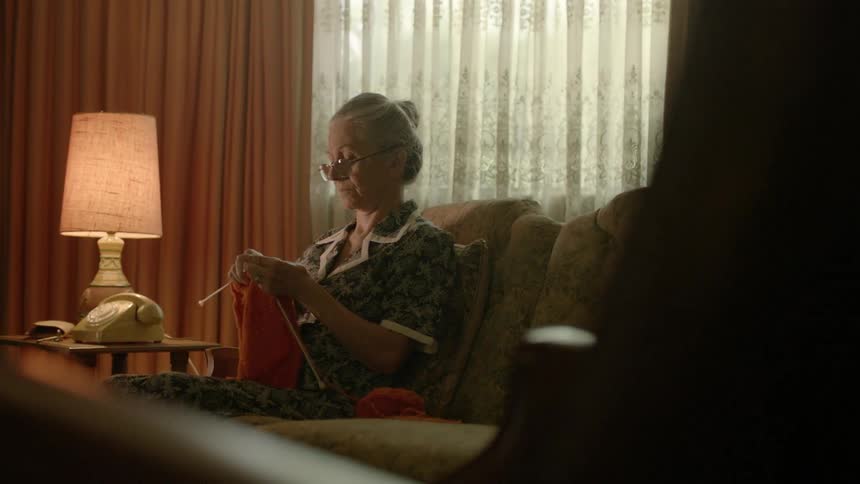 Woman knits while sitting on a couch next to a lamp