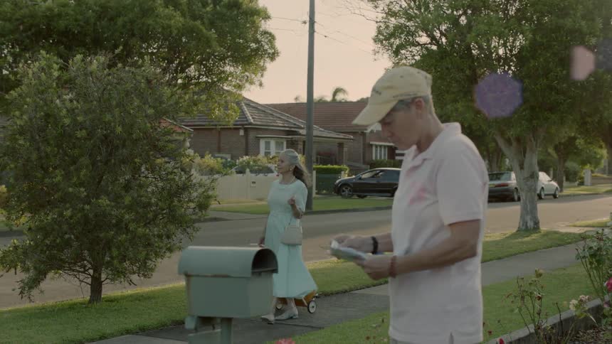 A woman is walking her dog while a man is checking the mail