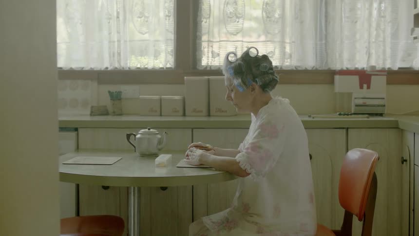 A woman sits at a table drinking from a mug