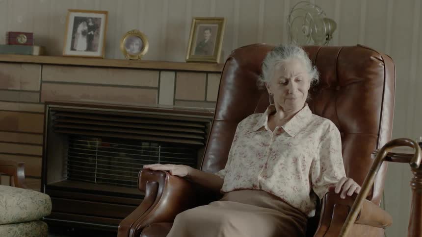 An old woman sits back in a leather recliner in a living room