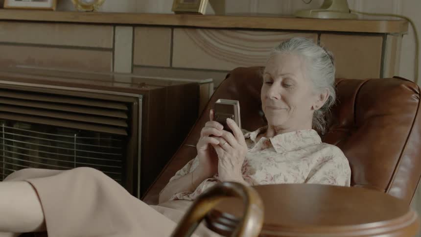 An older woman is laying back in her chair and watching tv
