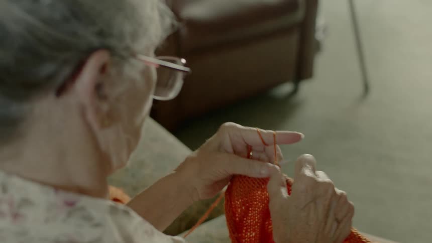 An old woman is sitting in a living room knitting
