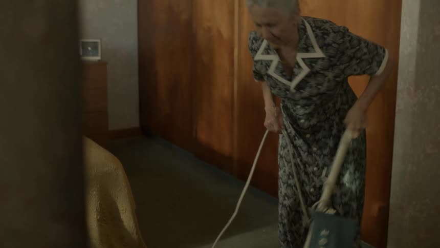 An older woman is vacuuming her bedroom