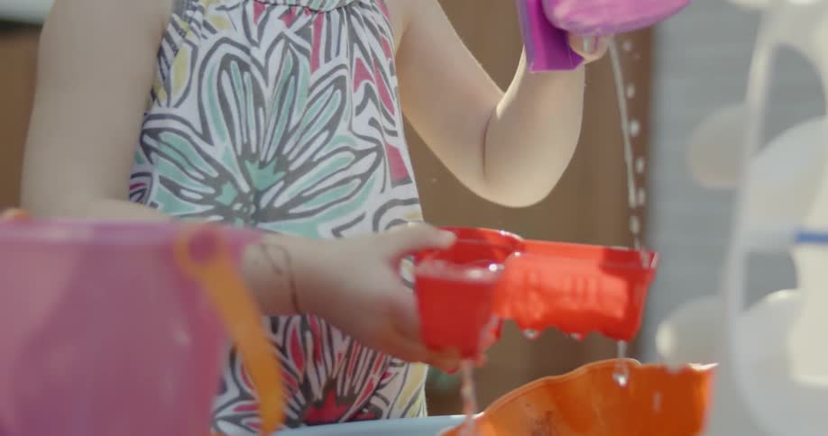 A girl is pouring water between containers outside during the day