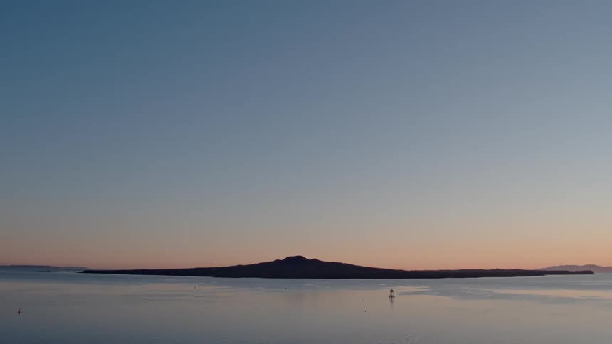 The sun sets behind a small bit of land in water