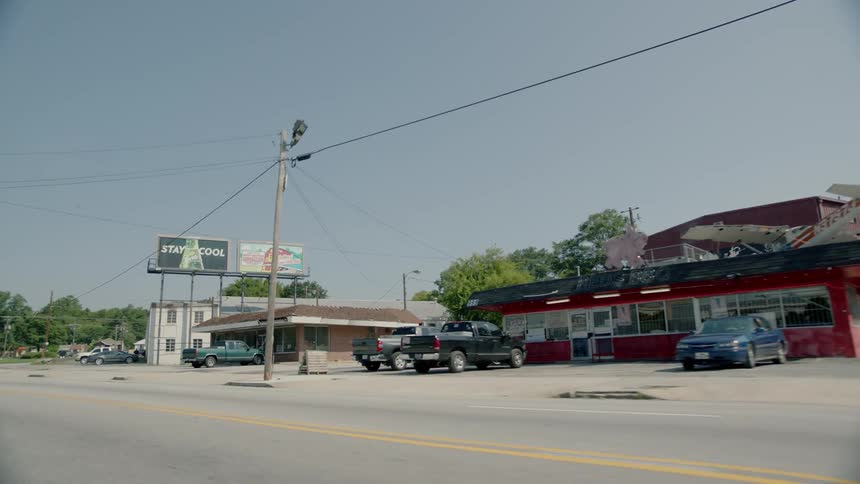 Vehicles sit outside shops in a town during the day