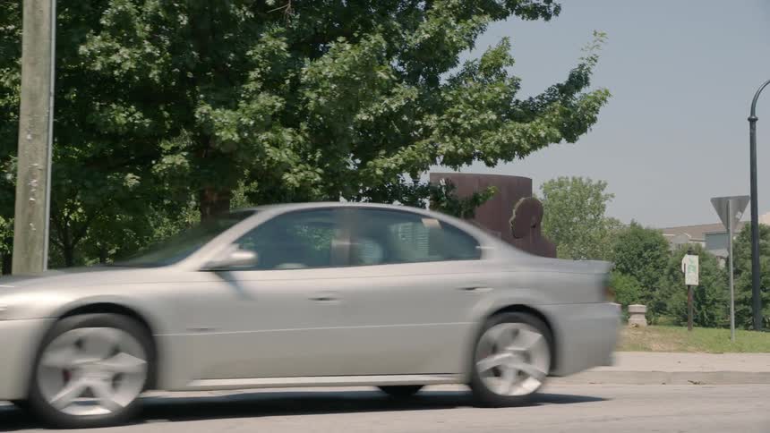 A park is filmed from a car on a busy street