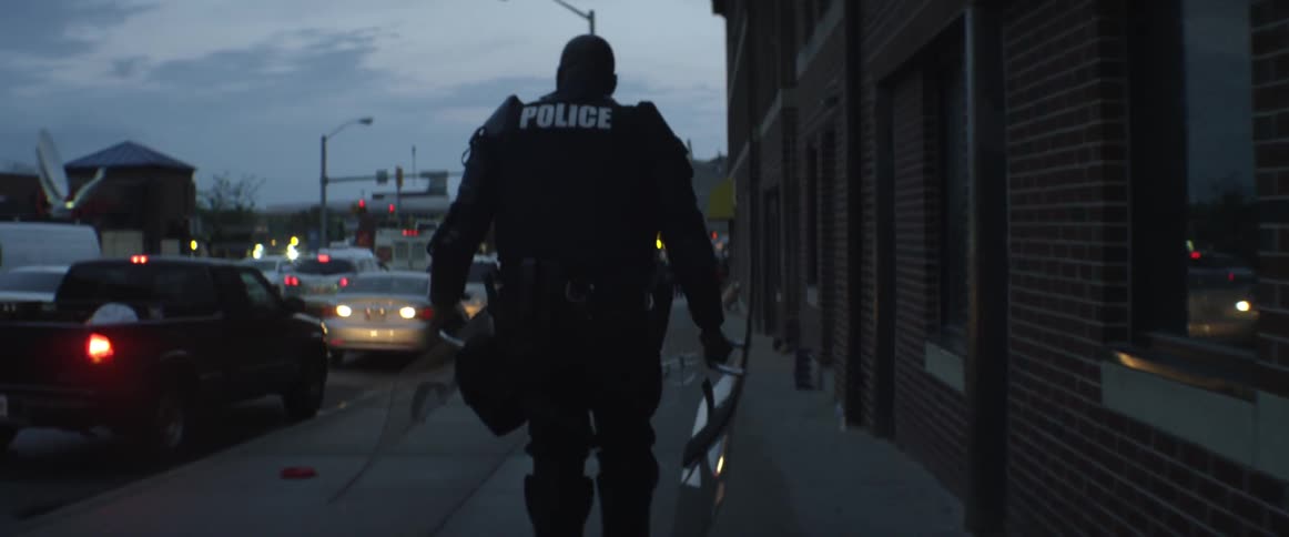 A policeman in full riot gear walks along a city sidewalk