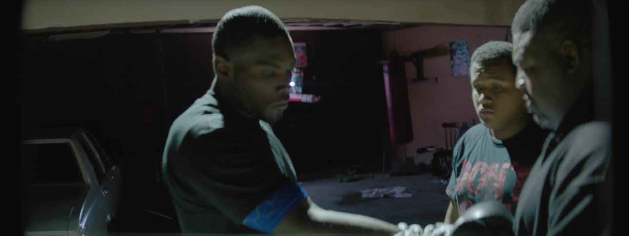 A trainer laces up a boxer's glove while another looks on