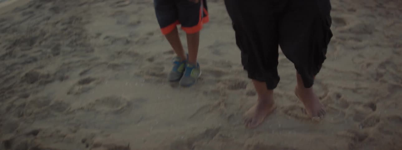 A man and his children are walking on a beach at sunset