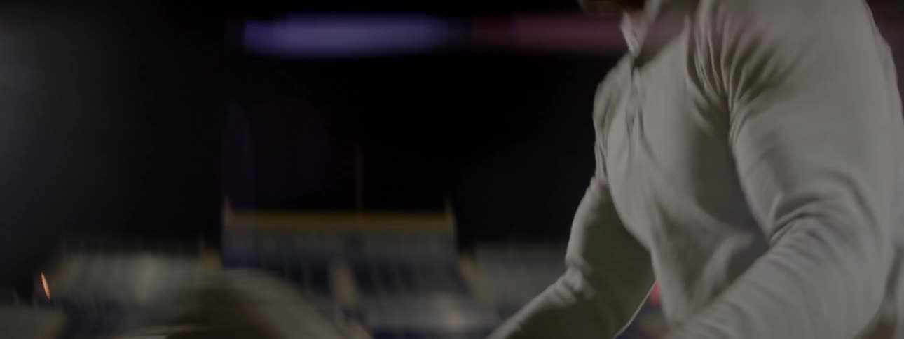 A man in sweats is flipping a large tire on a football field