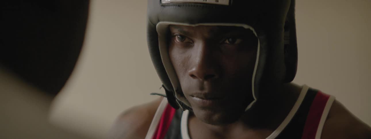 A boxer with a helmet on is getting advice from his corner