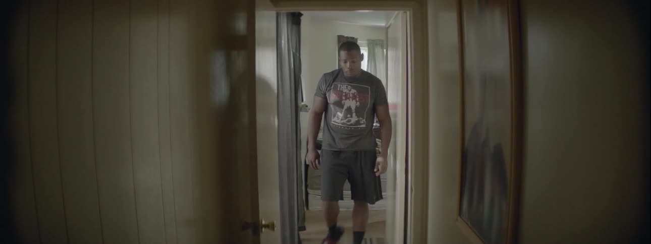 A man gets up from his bed and walks down a hallway to look at a picture