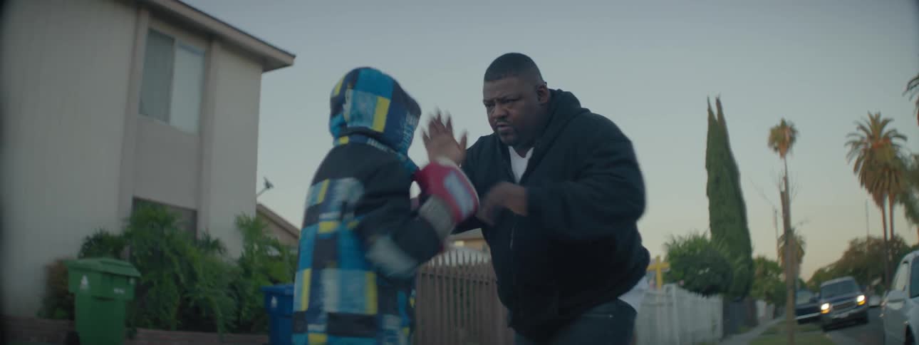 A man teaches a young boy to box on a front lawn