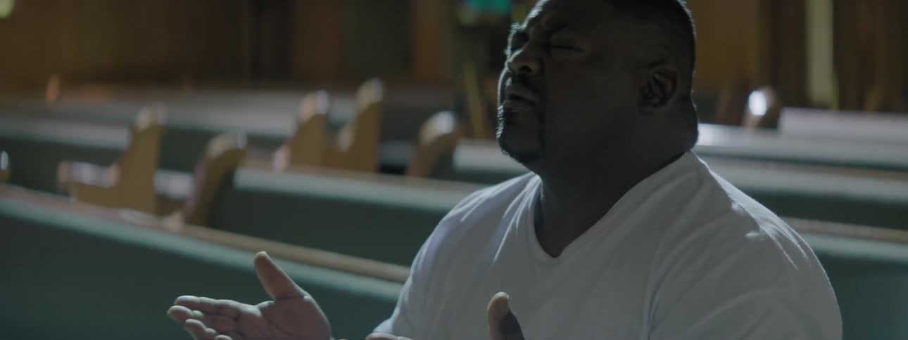 A man sits in a pew and prays with his hands open