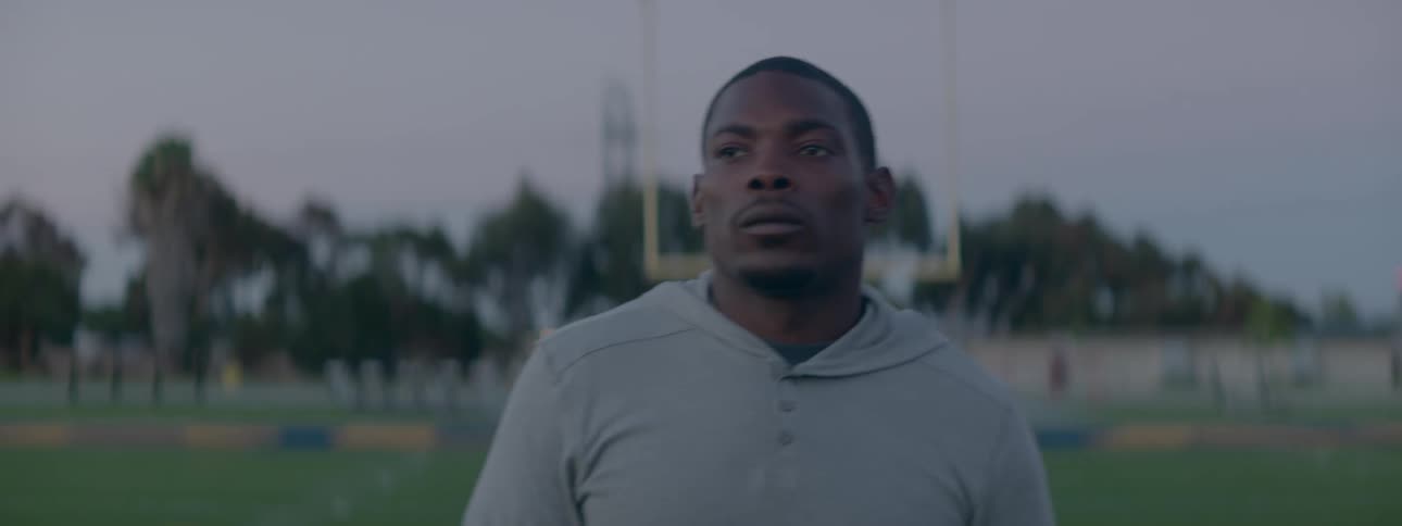 A man in sweats is walking on a football field