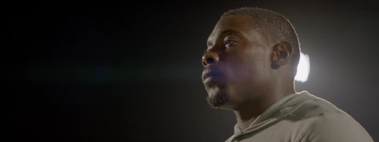 Man looking solemnly outdoors at night with a bright light shining behind them