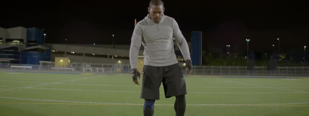 A man rolls a large tire across a football field