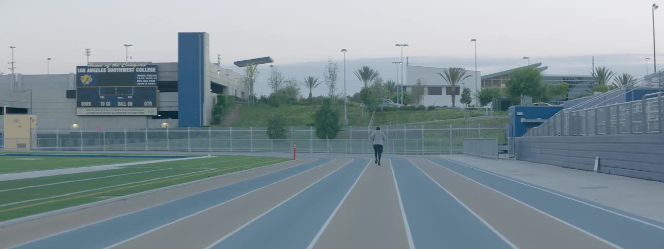 A man in sweats is running on a track next to a football field