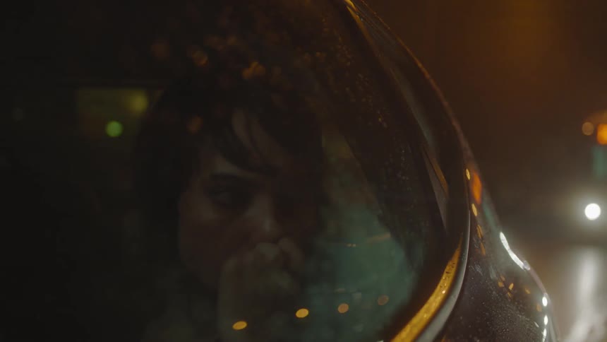 A woman is looking at her phone and out the window of a car as she rides in the backseat