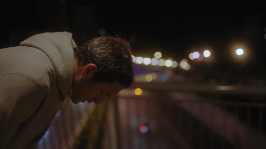 A man is bending over resting while on a bridge at night