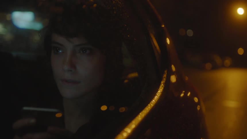 A female passenger in a car at night looks at her cellphone